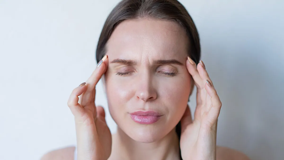 Mulher com enxaqueca segurando as têmporas de olhos fechados